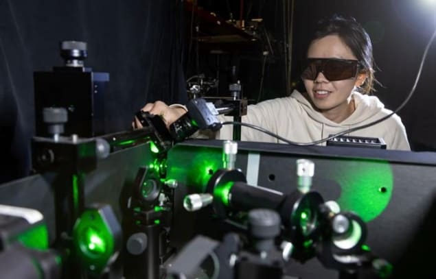 Photo of Genghua Yan wearing protective laser goggles as she manipulates equipment in the laboratory