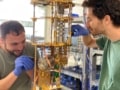 Photo of a smiling, protective glove-wearing Ofir Milul and Barkay Guttel with their dilution refrigerator