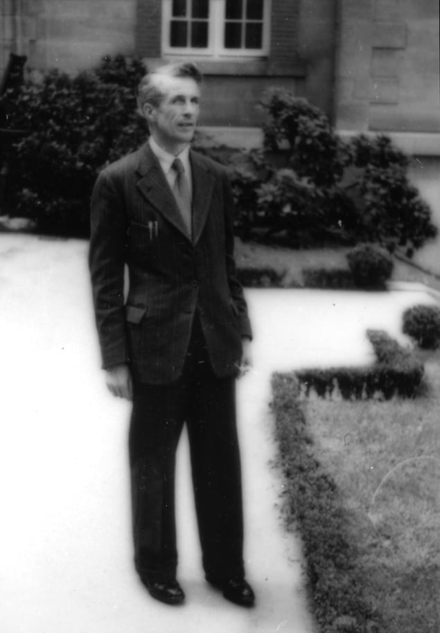 Ασπρόμαυρη φωτογραφία ενός άνδρα με κοστούμι έξω από ένα μεγάλο σπίτι