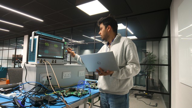Ένας άντρας με κουκούλα εργάζεται με ένα φορητό υπολογιστή και ένα κβαντικό σύστημα