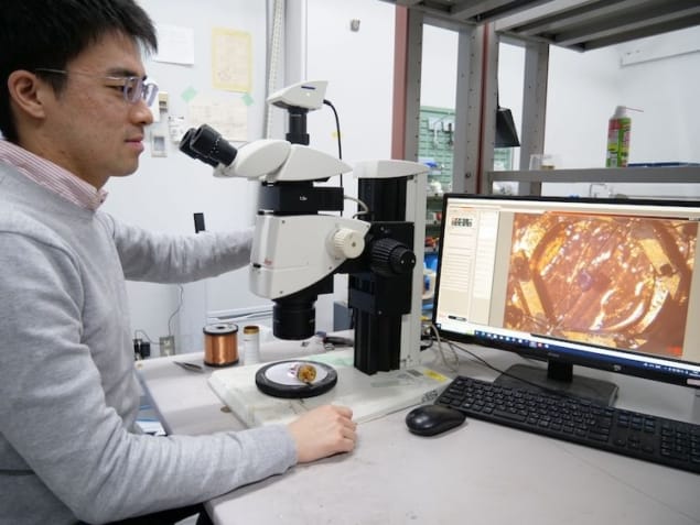 Fénykép Takasada Shibauchiról a laboratóriumában, amint egy képernyőt néz a mikroszkóp mellett