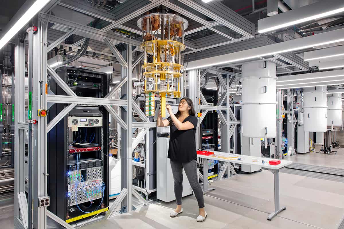 Ein Computerlabor mit einem Quantencomputer, der an einem Metallrahmen hängt, und einem Wissenschaftler, der etwas an seiner Basis justiert