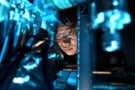 नीली रोशनी में नहाए हुए माइक्रोस्कोप का उपयोग कर रहे एक व्यक्ति की तस्वीर